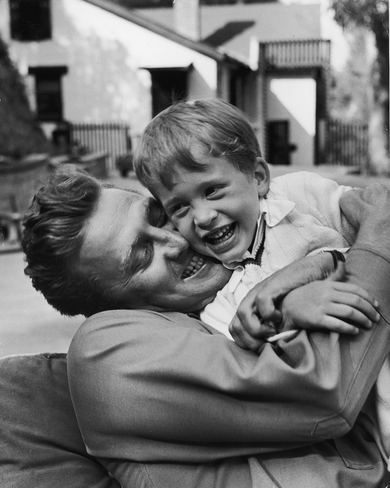 Actor Kirk Douglas hugging son Michael, who is laughing.
