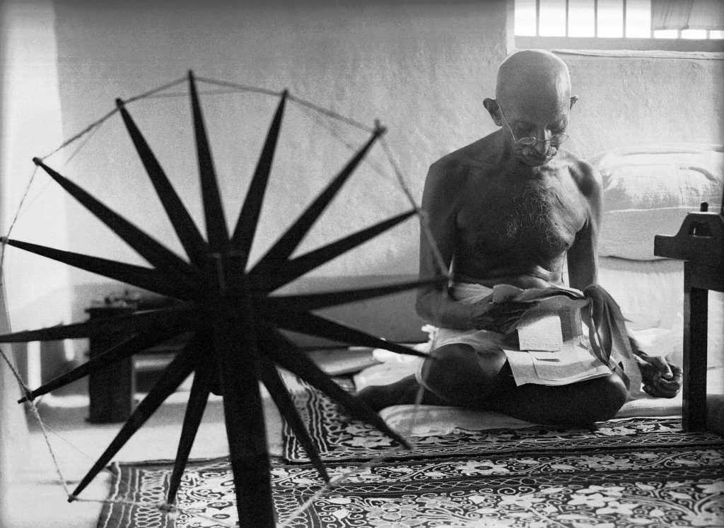 Indian leader Mohandas Gandhi reading next to a spinning wheel at home. (Photo by Margaret Bourke-White/The LIFE Picture Collection © Meredith Corporation)