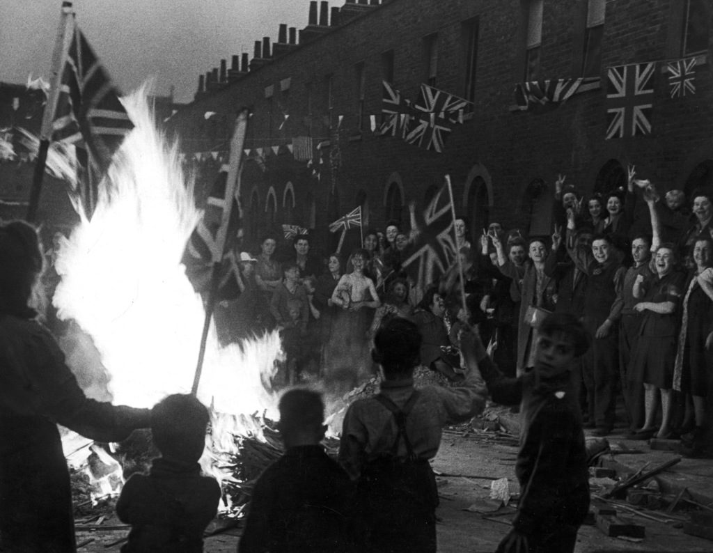 A crowd of joyous Britons wave flags around a bonfire built of material from bomb-wrecked homes as they celebrate the end of WWII in Europe following the surrender of Germany, London, England, May 8, 1945. (Photo by Leonard McCombe/The LIFE Images Collection)