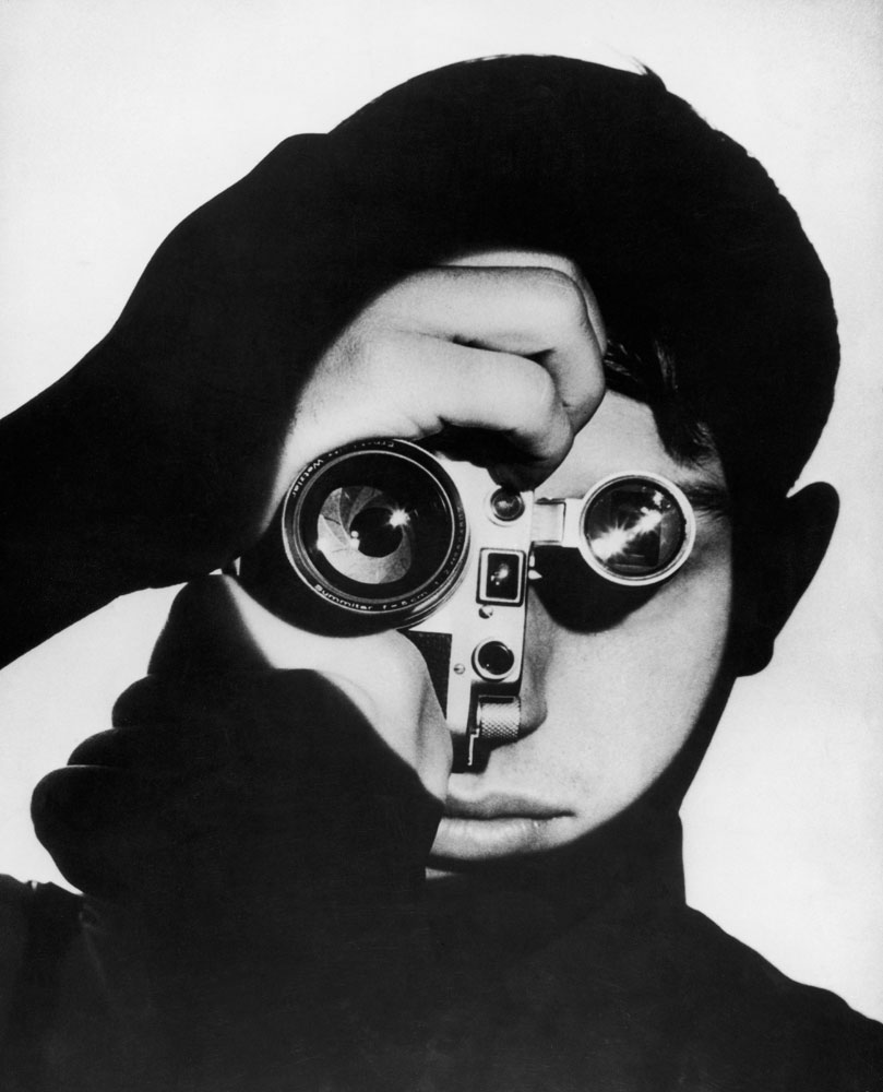 Photographer Dennis Stock holds a camera in front of his face, 1955.