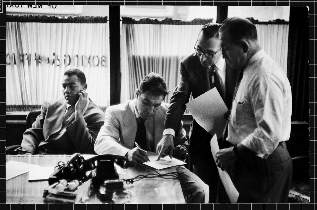 Boxer Rocky Marciano (seated R) signing a contract for a fight while Joe Louis (seated L) looks the other way. (Photo by Al Fenn/The LIFE Picture Collection © Meredith Corporation)