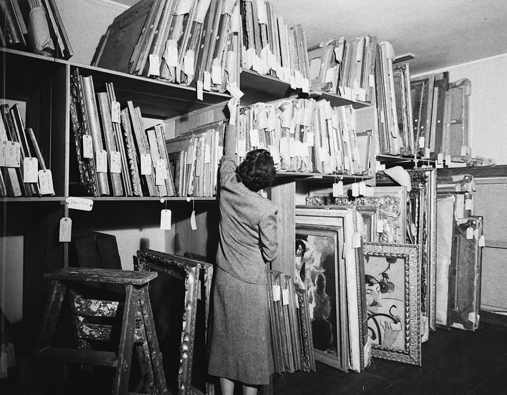 An unidentified woman looks at the tag on one of many paintings in a storage room in the home of financier and art collector Chester Dale, New York, New York, 1938. (Photo by Rex Hardy/The LIFE Picture Collection © Meredith Corporation)
