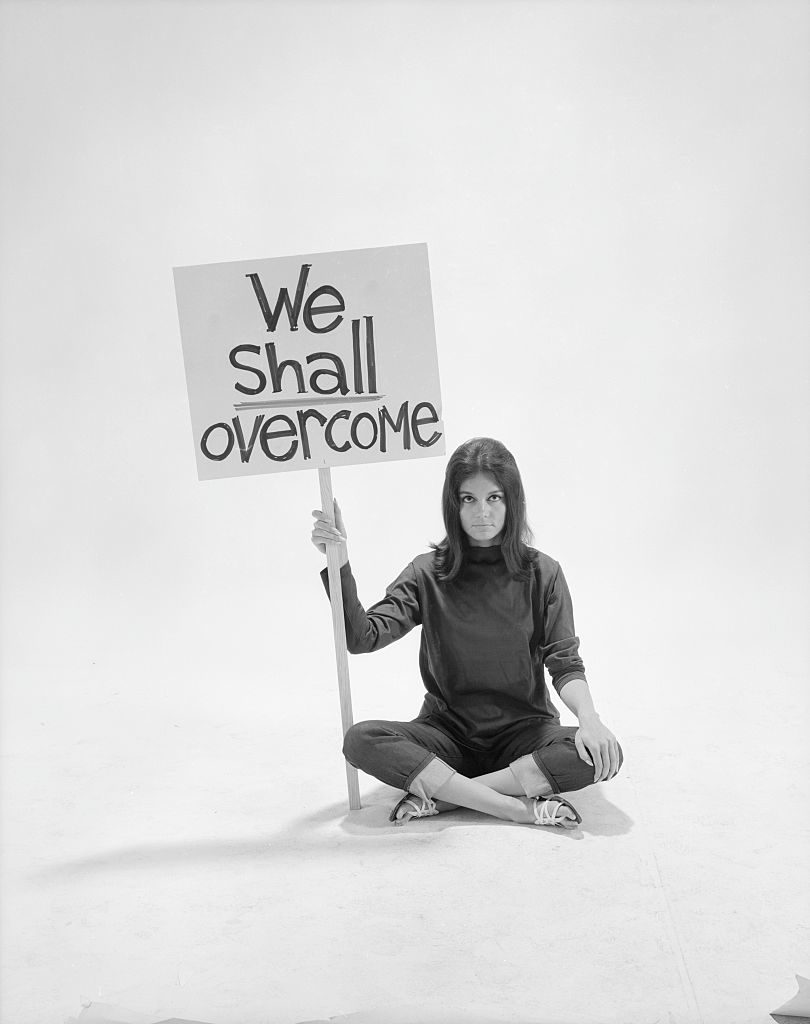 Writer Gloria Steinem sitting cross-legged on floor w. sign We Shall Overcome re pop culture (Photo by Yale Joel/The LIFE Picture Collection © Meredith Corporation)