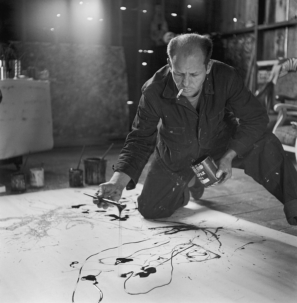 Painter Jackson Pollock smoking as he squats on floor, applying paint to canvas in Long Island studio. (Photo by Martha Holmes/The LIFE Picture Collection © Meredith Corporation)