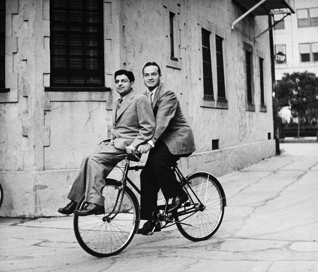 Columnist Sidney Skolsky (L) catching a ride on Bob Hope's (R) bicycle on his way from his dressing room to the sound stage. (Photo by John Florea/The LIFE Picture Collection © Meredith Corporation)