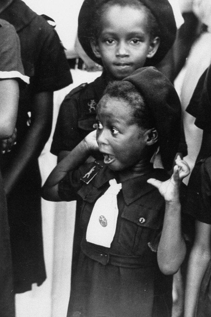 A Jamaican girl scout with surprised look as she watches the arrival of Queen Elizabeth II. Jamaica, 1953.