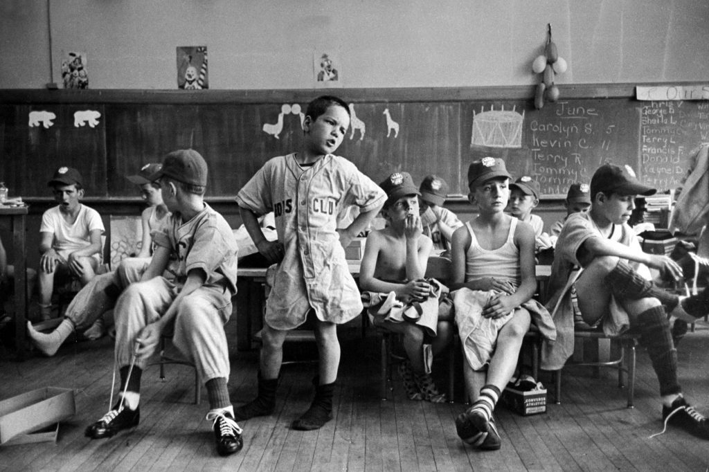 Group of Boys Club little league baseball players putting on their uniforms while sitting in classroom, Manchester, NH, 1954.
