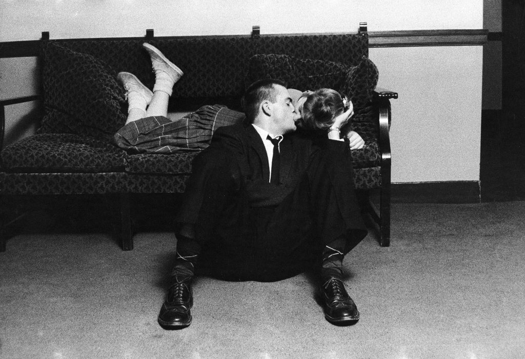 A University of Michigan student couple engaged in an impromptu kiss in the Union Building on campus. 1957. This was forbidden conduct because rules required couples to have both feet on the floor.