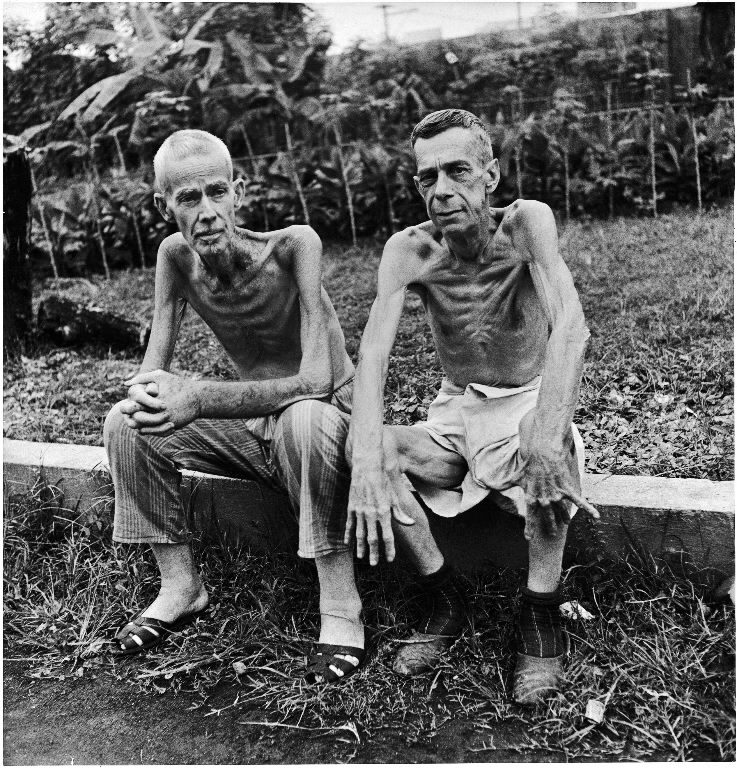 Two emaciated American civilians, Lee Rogers (L) and John C. Todd, sitting outside a Japanese prison camp following their release by Allied forces liberating the city. (Photo by Carl Mydans/The LIFE Picture Collection © Meredith Corporation)