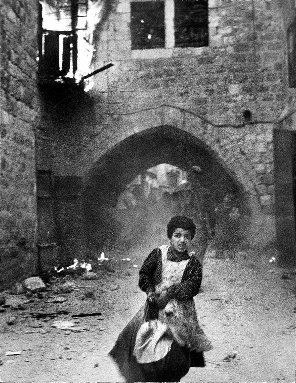 Terrified young Jewish girl Rachel Levy, 7, fleeing from a street with burning buildings as the Arabs sack the Holy City after its surrender during Palestinian Civil war. (Photo by John Phillips/The LIFE Picture Collection © Meredith Corporation)